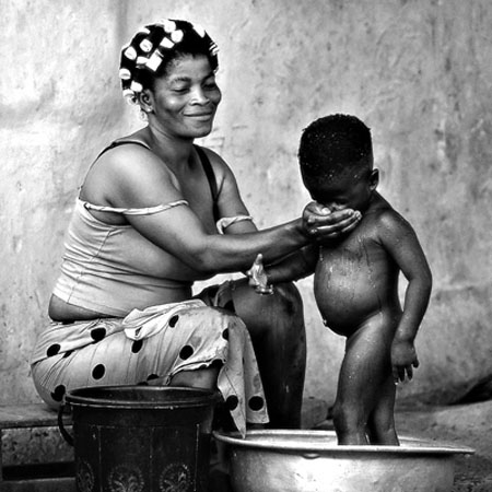 Mujer bañando a su hijo pequeño en un barreño de metal